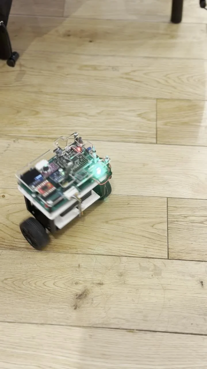 Frame from the prototype video showing the two-wheel robot moving across a wooden floor with its green indicator illuminated